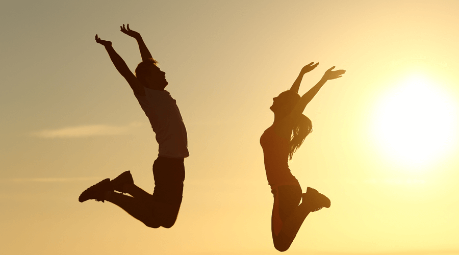 A man and a lady are jumping towards the sunlight and are happy enjoying themselves and their wellness